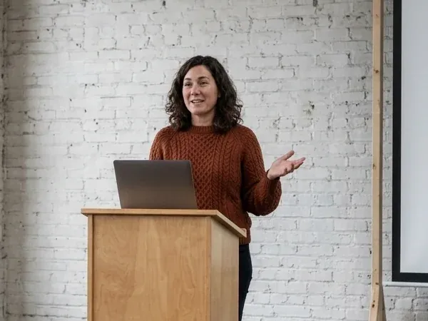 A speaker in a rust-coloured sweater at the lectern in the brick hall, mid-talk, at last year's map day