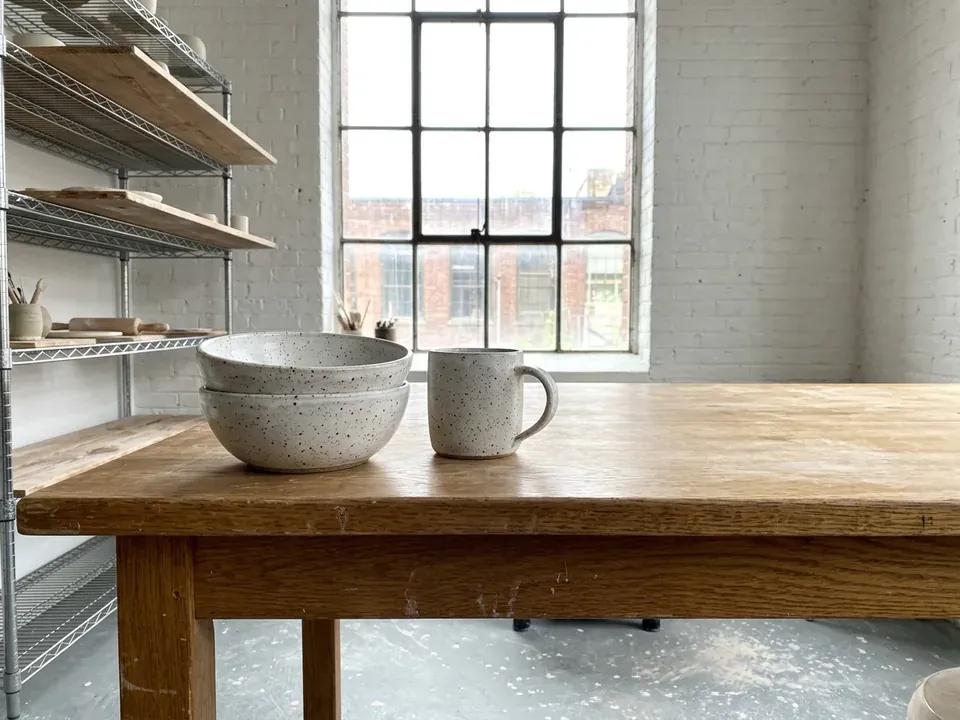 Two speckled white bowls and a mug on an oak table