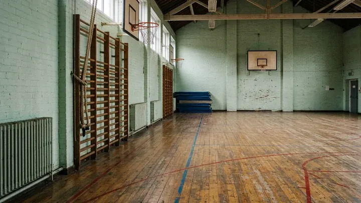 An empty old school sports hall with a worn wooden floor, wall bars and high windows