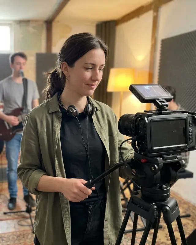 Dana Kowalczyk at her camera on a tripod, filming a band in a rehearsal room